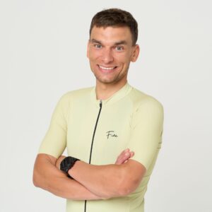 kolarz w koszulce kolarskiej stojący przodem do fotografa, z śmiechem