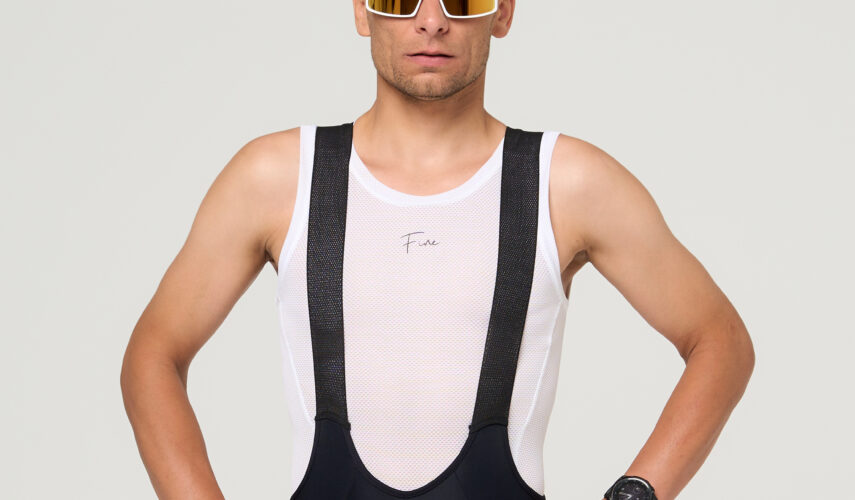 Stojący kolarz w czarnych spodenkach kolarskich oraz białej potówce kolarskiej